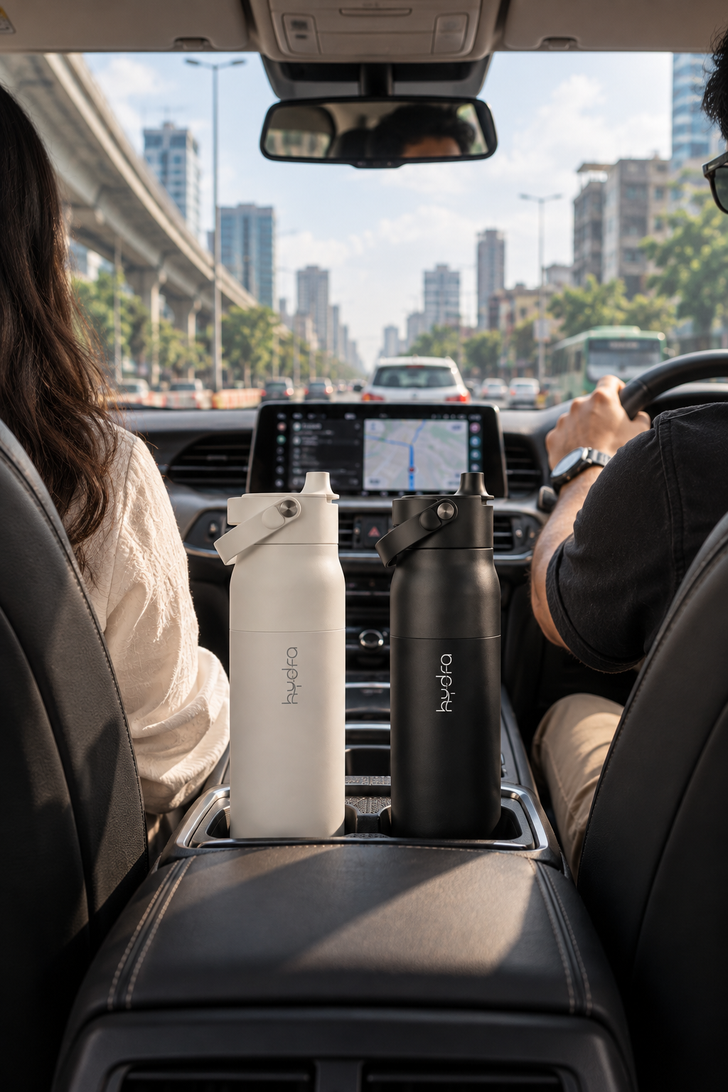 White and black Hydra bottles in a car’s centre console during a city commute.