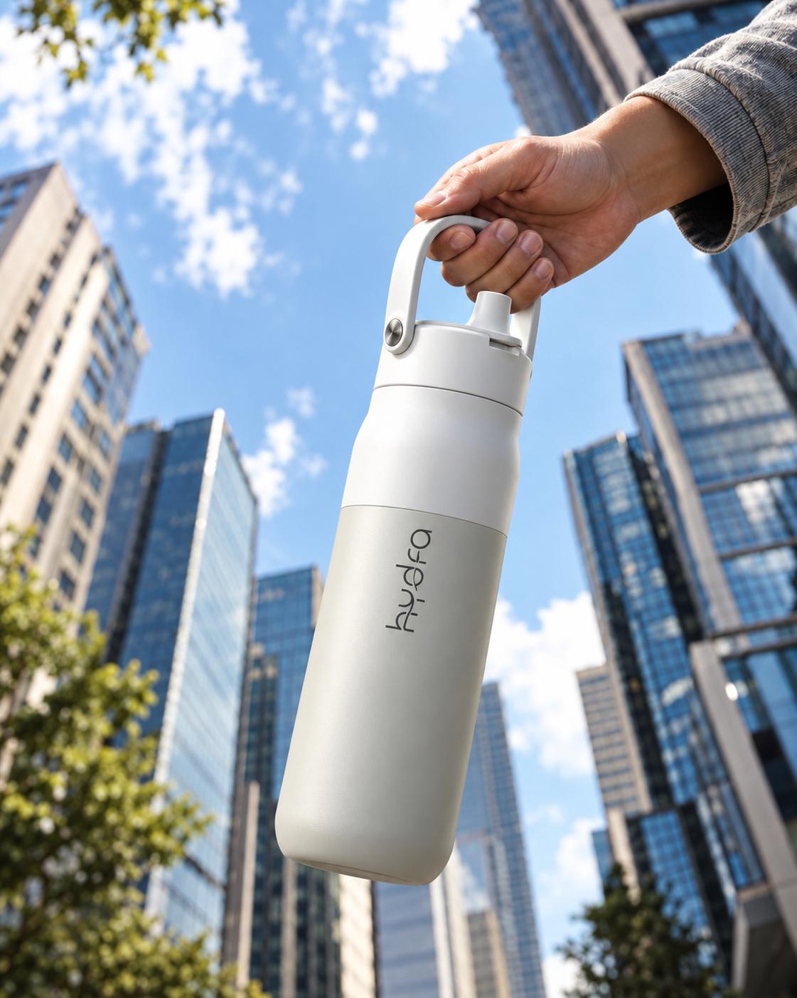 A white Hydra bottle carried by its handle against a city skyline